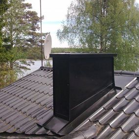 Tyylikäs musta pellitetty savupiippu maalaistalossa Porvoon alueella.